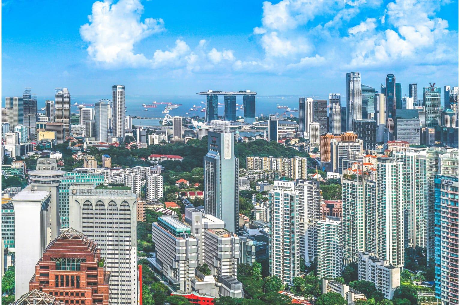 Aerial photo of Singapore skyline featuring buildings Guoco Tower and Marina Bay Sands with a bright blue sky.