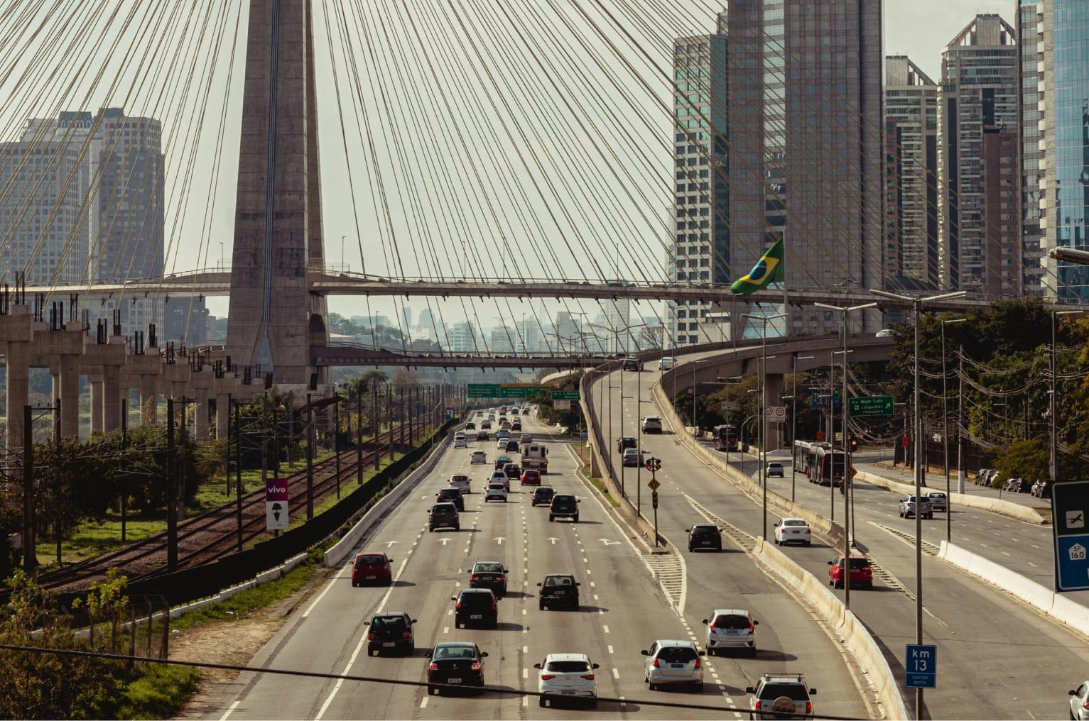 There are several cars driving along a busy highway. There is a grand bridge over the top of the motorway.