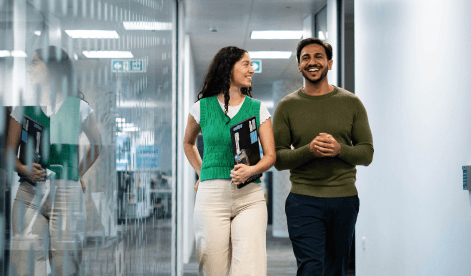 Two employees are smiling walking down a corridor