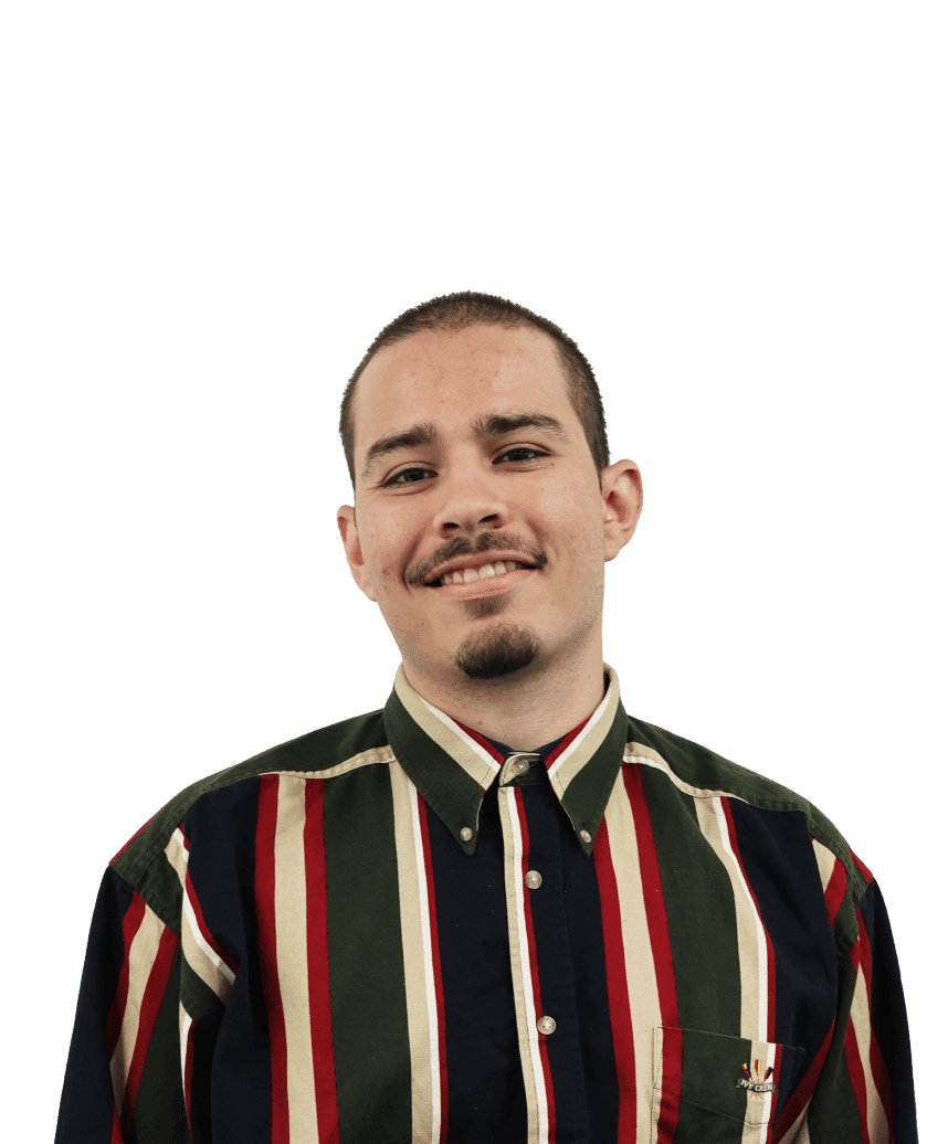 A man stands smiling into the camera wearing a striped vertical shirt, with a blurred background.