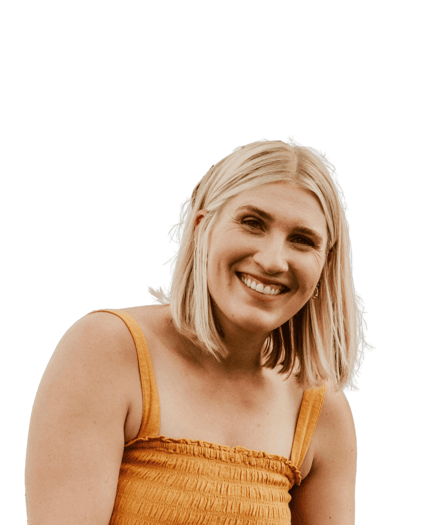 A woman wears an orange dress and smiles towards the camera, in front of a blurred background.