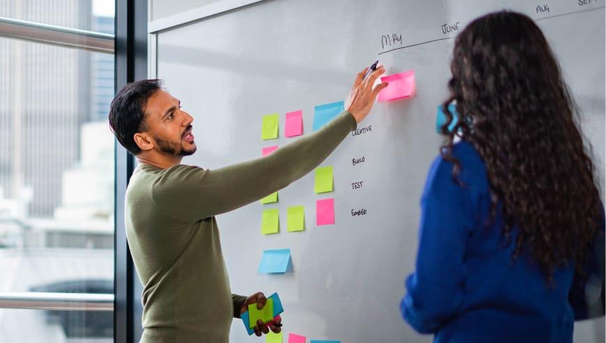 Man in an office placing sticky notes onto a whiteboard.