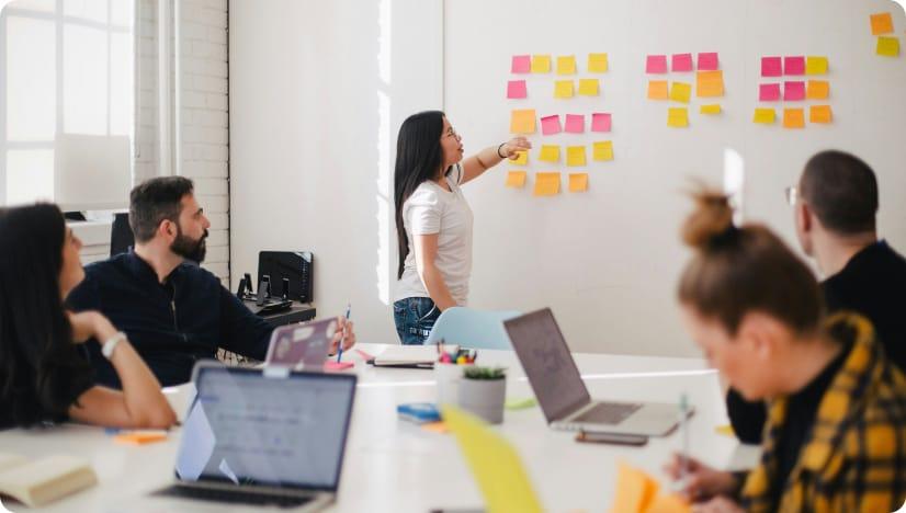 Group of people in an office space working on a whiteboard with sticky notes.