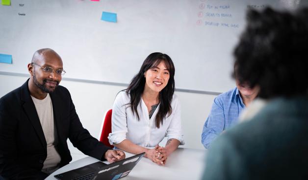 Group in a meeting room at a workplace sitting round a table smiling and learning