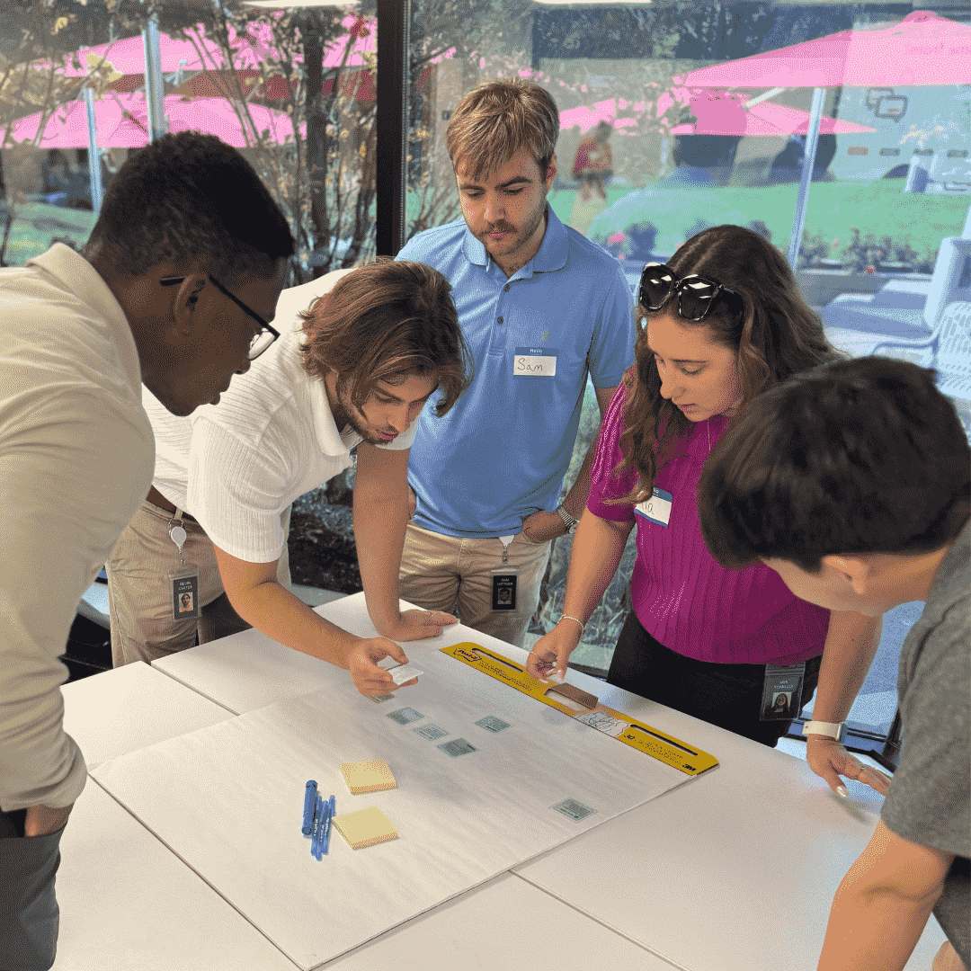 Five people at Worldpay stand around a table, collaborating with paper and cards near a large window.