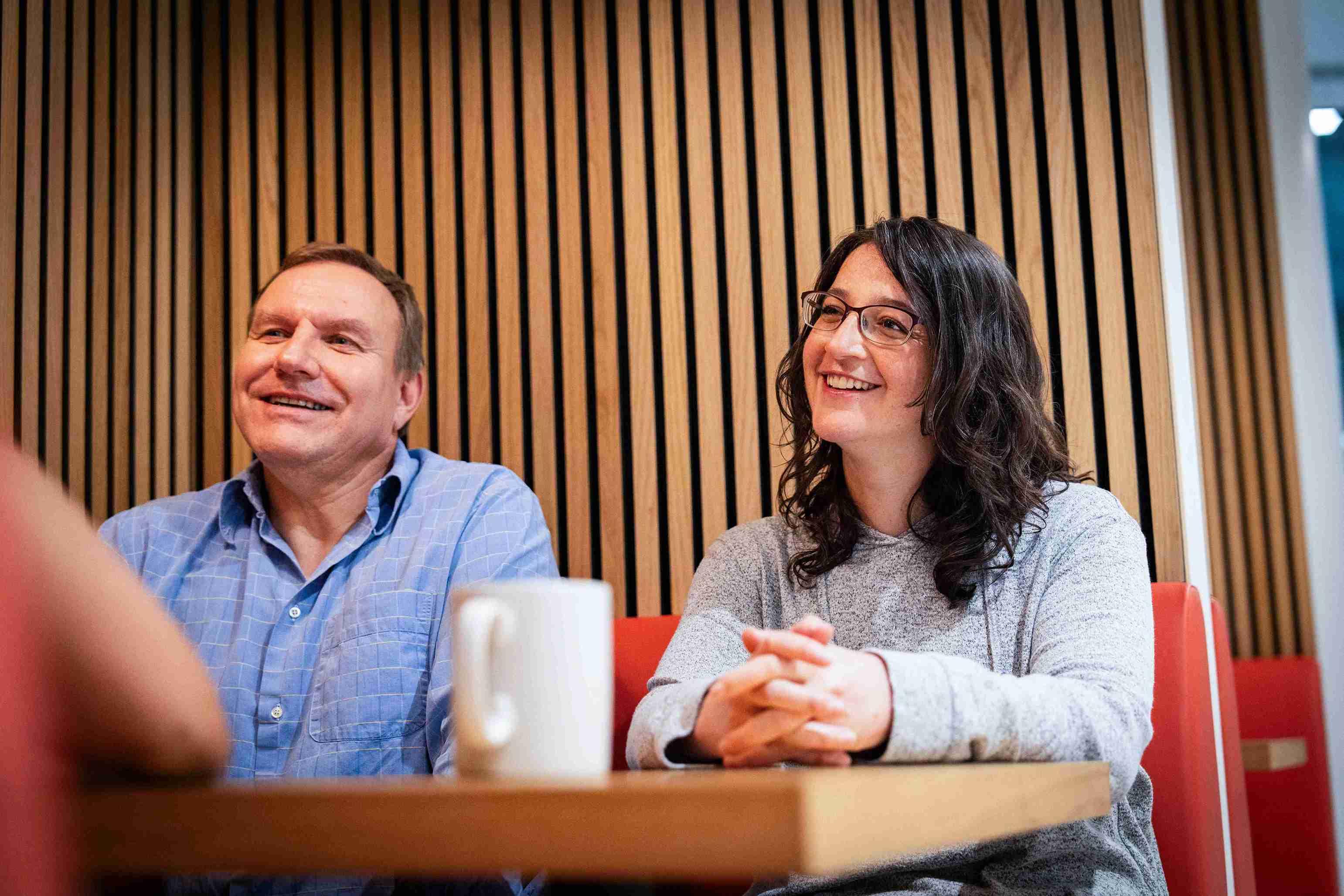 Man and women smiling having coffee sat at a table