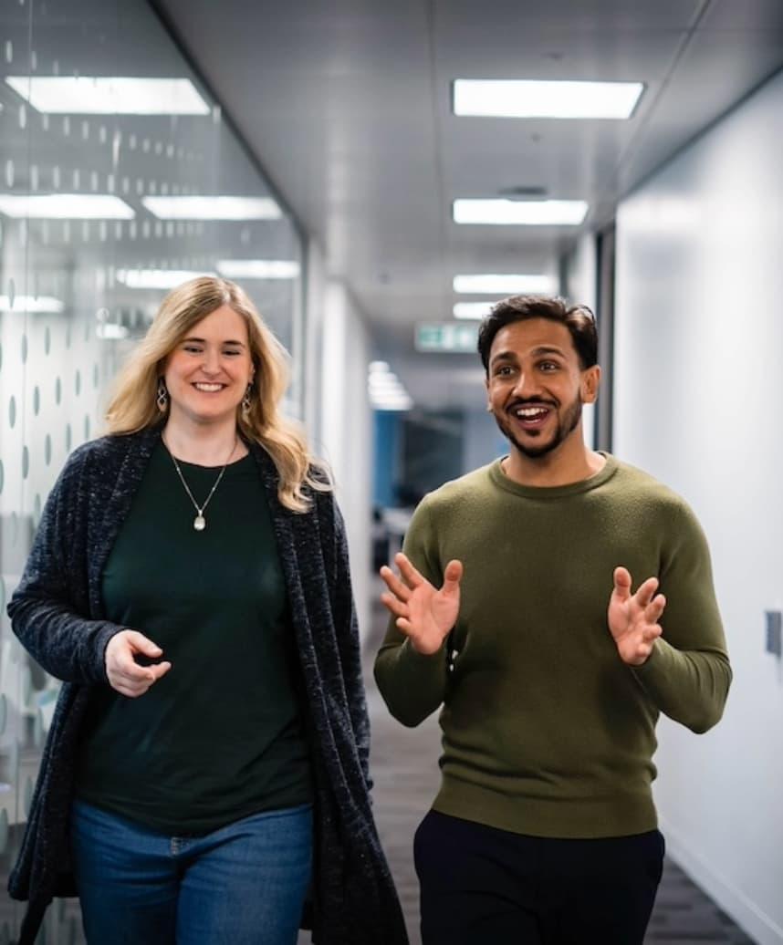 Two people walking through the office. They are both smiling