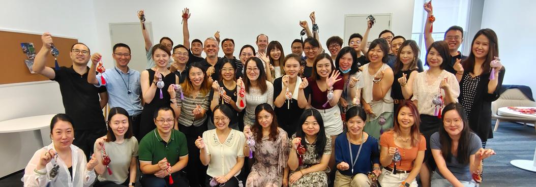 A large group of people in an office pose for a photo, each holding up a small paper lantern.