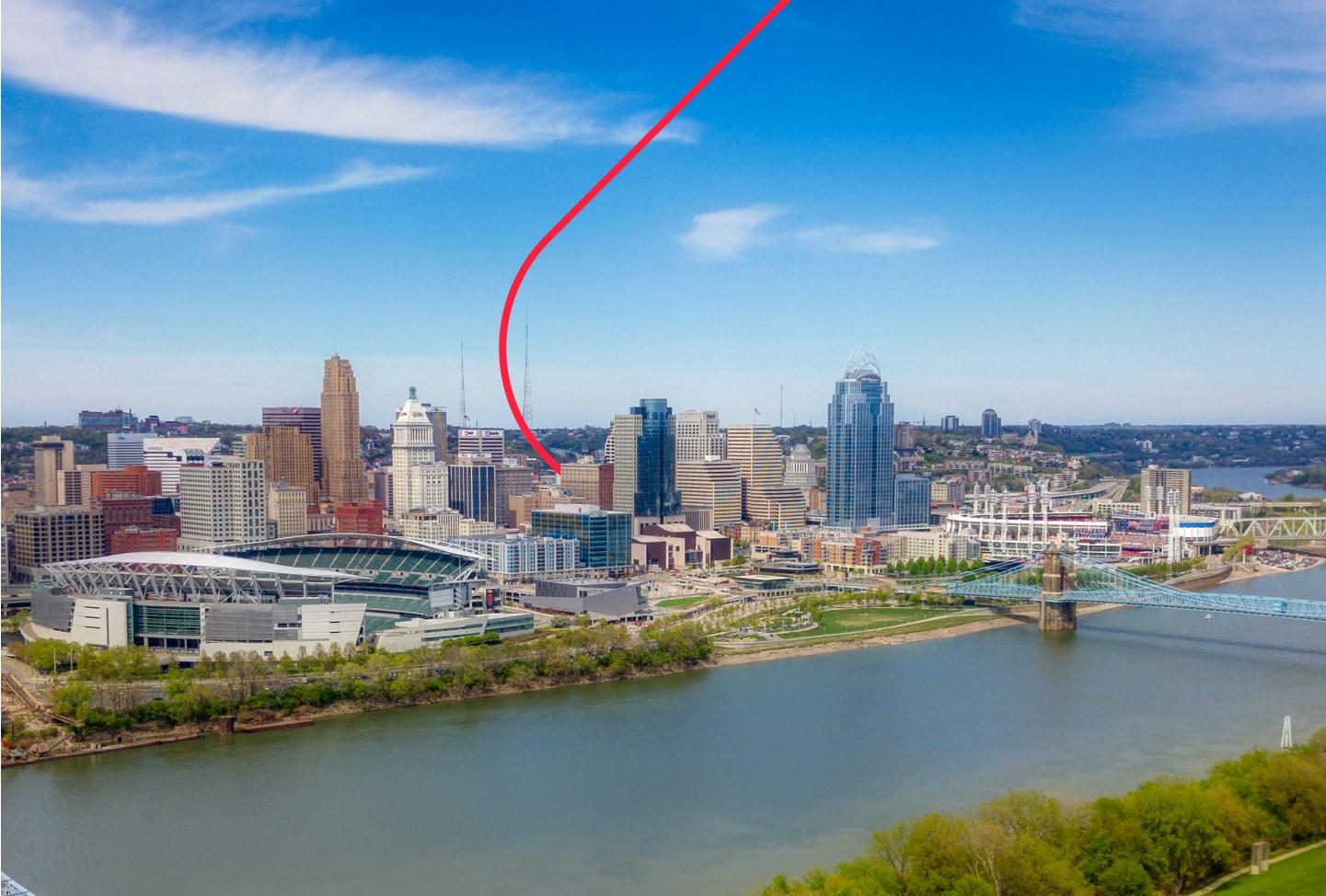 Aerial shot of the Great American Ball and the Park Paycor Stadium with the skyline in the background and river in the foreground.