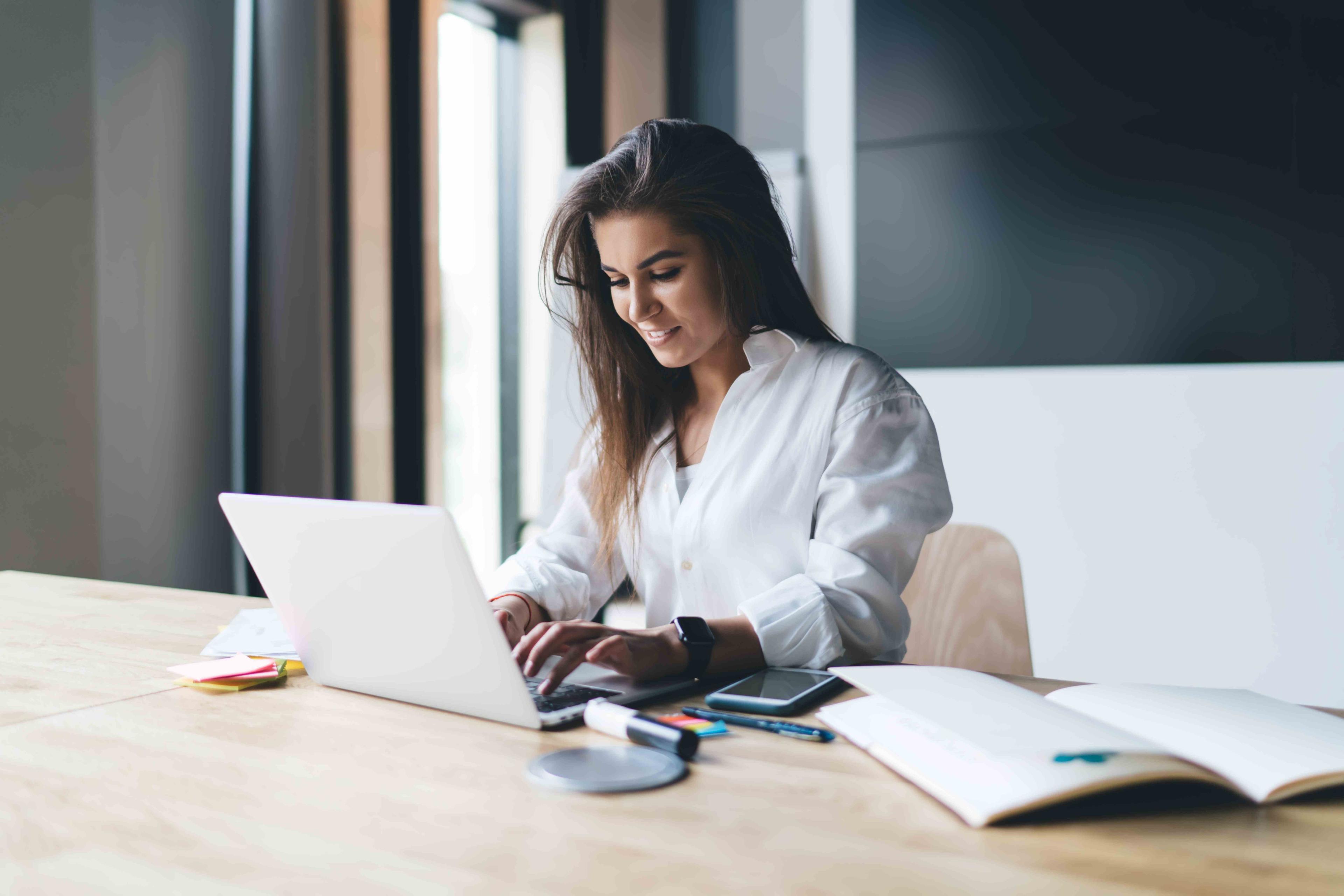 Woman in white shirt with dark hair working on laptop